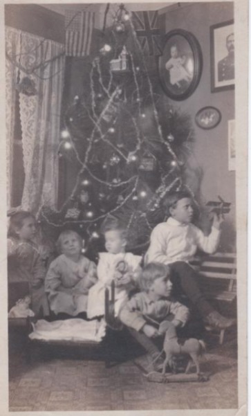 Old black and white photo of five children in front of a Christmas tree